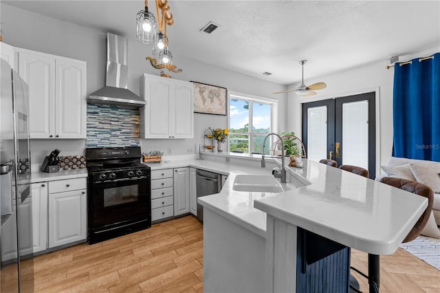 kitchen with kitchen peninsula, a breakfast bar, stainless steel appliances, sink, and wall chimney range hood