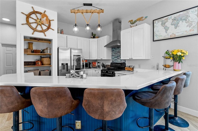 kitchen featuring wall chimney exhaust hood, black gas range, a kitchen breakfast bar, and stainless steel fridge with ice dispenser