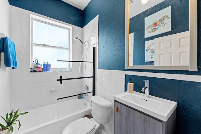 full bathroom featuring tiled shower / bath, vanity, toilet, and tile walls