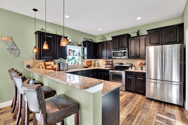 kitchen featuring light stone countertops, light hardwood / wood-style flooring, kitchen peninsula, decorative light fixtures, and appliances with stainless steel finishes