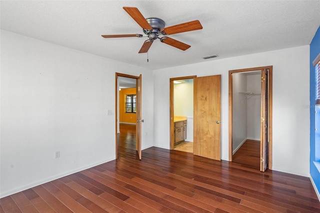 unfurnished bedroom with ensuite bath, ceiling fan, dark wood-type flooring, a spacious closet, and a closet