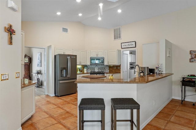 kitchen with high vaulted ceiling, white cabinets, dark stone countertops, appliances with stainless steel finishes, and kitchen peninsula