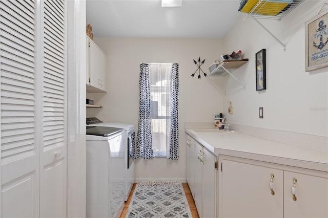 clothes washing area with light hardwood / wood-style floors, sink, cabinets, and independent washer and dryer