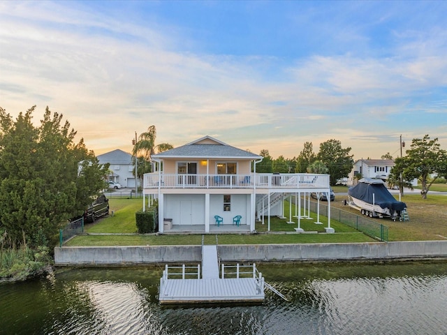 back house at dusk featuring a deck with water view, a patio area, and a lawn