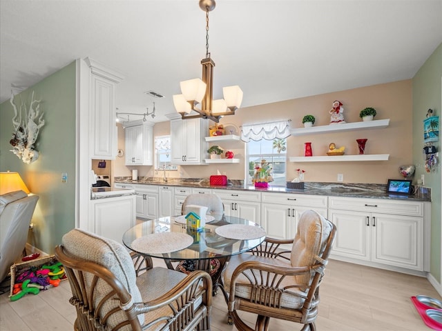 kitchen with white cabinetry, hanging light fixtures, sink, light hardwood / wood-style flooring, and an inviting chandelier