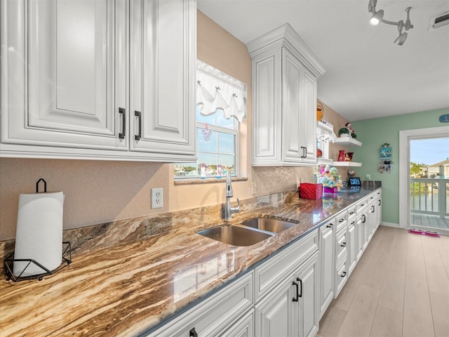 kitchen with white cabinets, dark stone counters, light hardwood / wood-style flooring, and sink