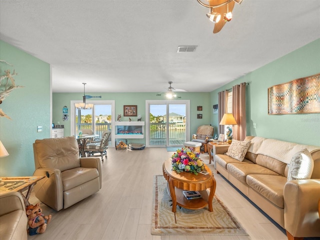 living room with ceiling fan with notable chandelier, a textured ceiling, and light hardwood / wood-style flooring