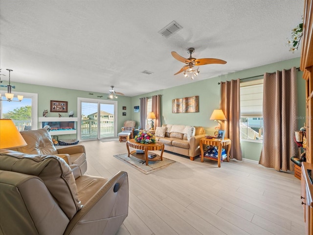 living room featuring ceiling fan with notable chandelier, a textured ceiling, and light hardwood / wood-style flooring