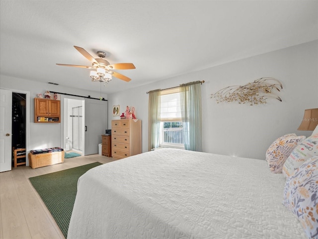 bedroom featuring ceiling fan, a barn door, and light hardwood / wood-style floors