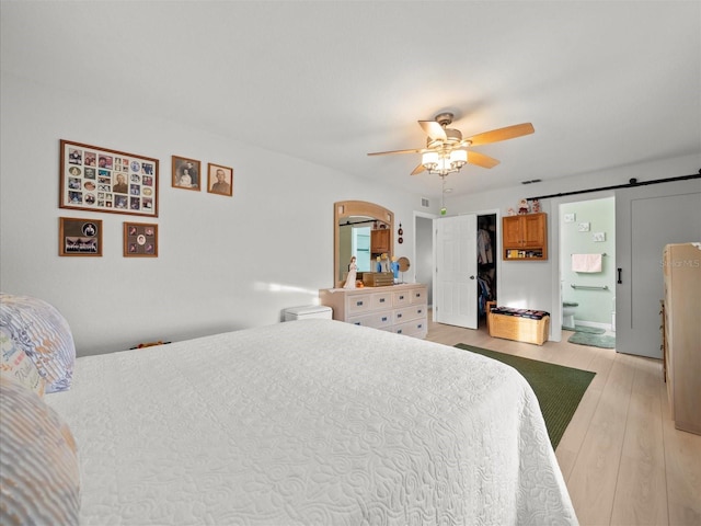 bedroom featuring ensuite bathroom, light wood-type flooring, ceiling fan, and a barn door