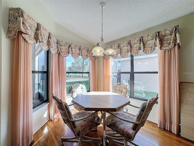 dining space with hardwood / wood-style flooring, a textured ceiling, and vaulted ceiling