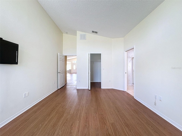 unfurnished bedroom featuring a walk in closet, a textured ceiling, high vaulted ceiling, dark hardwood / wood-style floors, and a closet