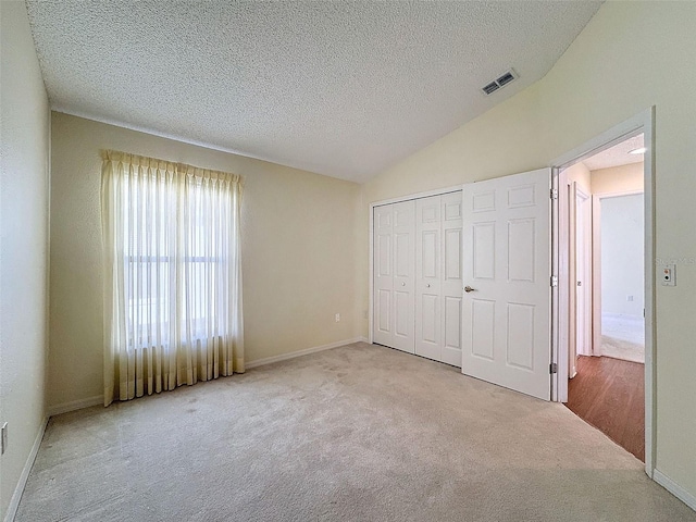 unfurnished bedroom featuring lofted ceiling, light carpet, a closet, and a textured ceiling