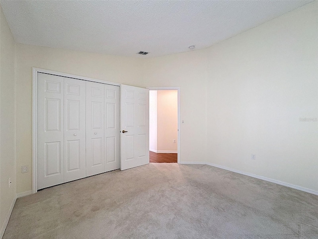 unfurnished bedroom featuring light carpet, a textured ceiling, and a closet