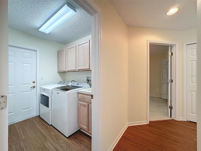 laundry room with cabinets, wood-type flooring, a textured ceiling, and washing machine and clothes dryer