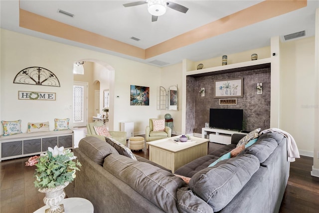 living room with a raised ceiling, ceiling fan, and dark hardwood / wood-style flooring