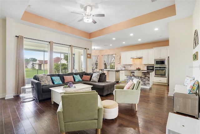 living room with a raised ceiling, ceiling fan, and dark wood-type flooring