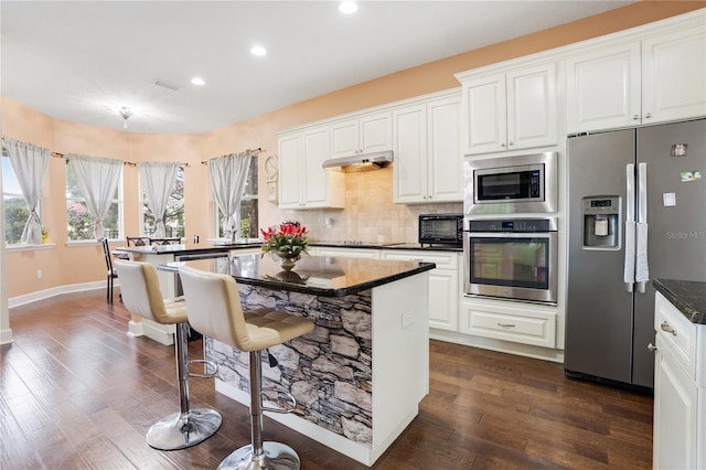 kitchen with dark hardwood / wood-style floors, backsplash, dark stone counters, white cabinets, and appliances with stainless steel finishes