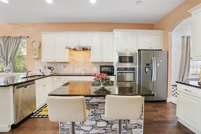 kitchen with dark stone counters, stainless steel appliances, sink, a center island, and white cabinetry