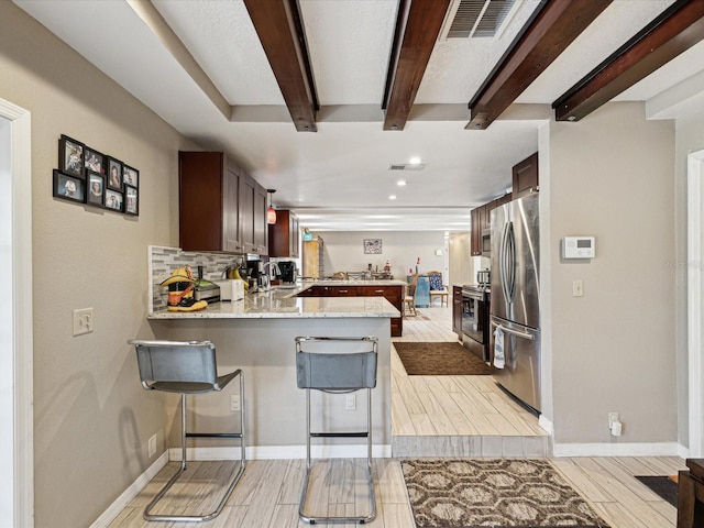 kitchen featuring a breakfast bar, decorative backsplash, light stone countertops, kitchen peninsula, and stainless steel refrigerator