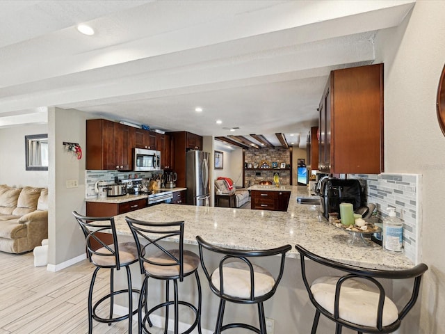 kitchen with kitchen peninsula, appliances with stainless steel finishes, light wood-type flooring, tasteful backsplash, and sink