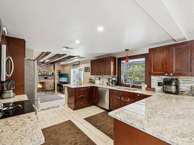 kitchen with kitchen peninsula, appliances with stainless steel finishes, light stone counters, a brick fireplace, and hanging light fixtures