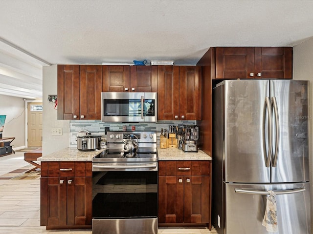 kitchen featuring a textured ceiling, light stone counters, stainless steel appliances, and tasteful backsplash