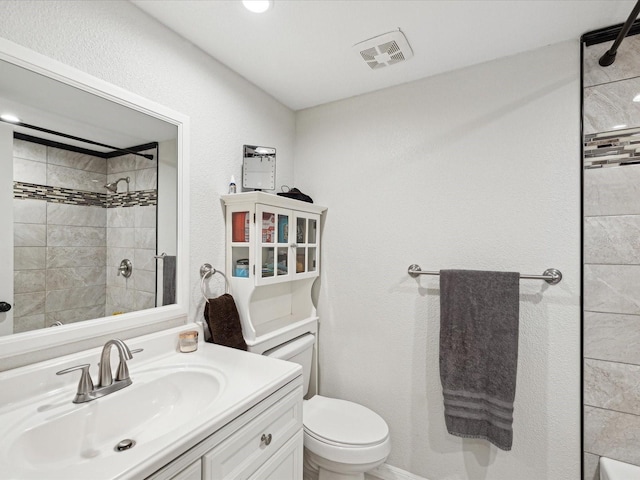 bathroom with vanity, toilet, and tiled shower