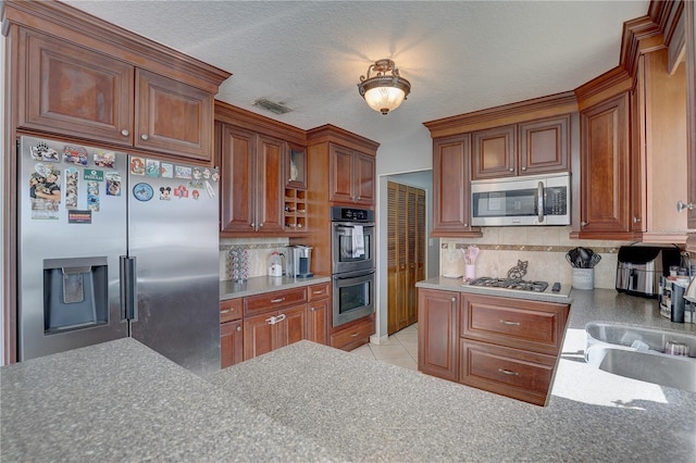 kitchen with sink, decorative backsplash, a textured ceiling, appliances with stainless steel finishes, and light tile patterned flooring