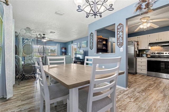 dining space featuring ceiling fan with notable chandelier, light wood-type flooring, and a textured ceiling