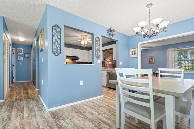 dining area with ceiling fan with notable chandelier, sink, light wood-type flooring, and a textured ceiling