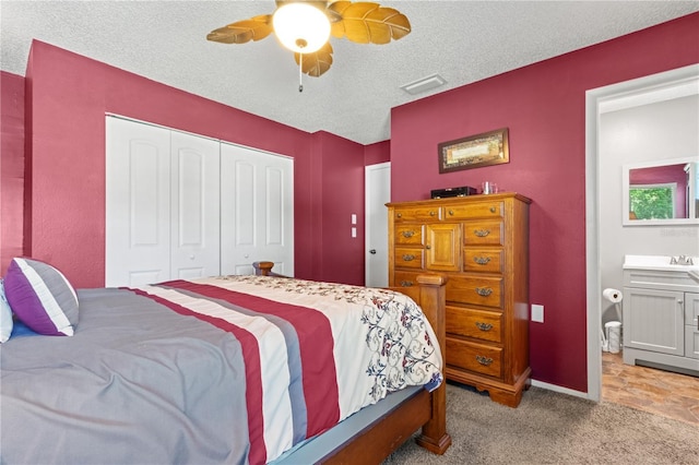 bedroom featuring connected bathroom, ceiling fan, a textured ceiling, light carpet, and a closet