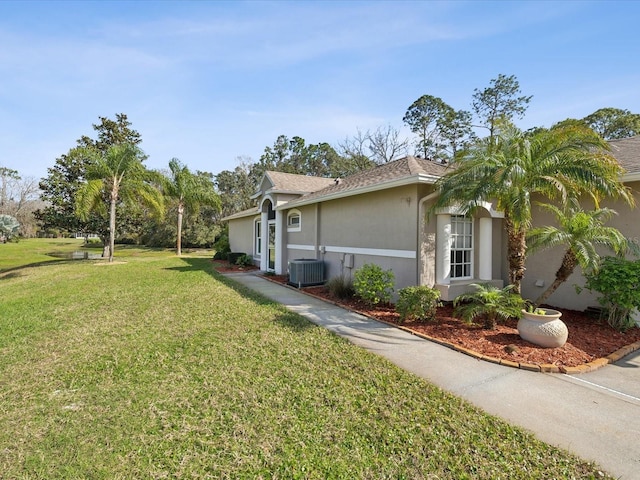 view of side of property featuring stucco siding, central AC unit, and a yard