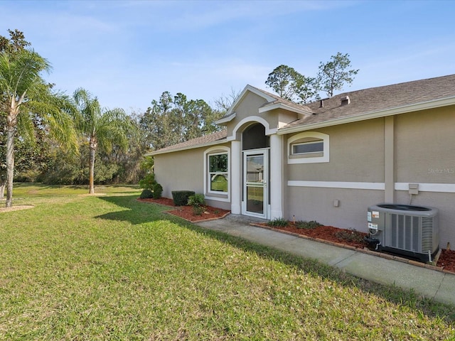 view of front of property featuring stucco siding, central AC unit, and a front yard