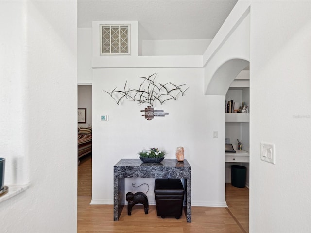 hallway featuring arched walkways, wood finished floors, visible vents, and baseboards