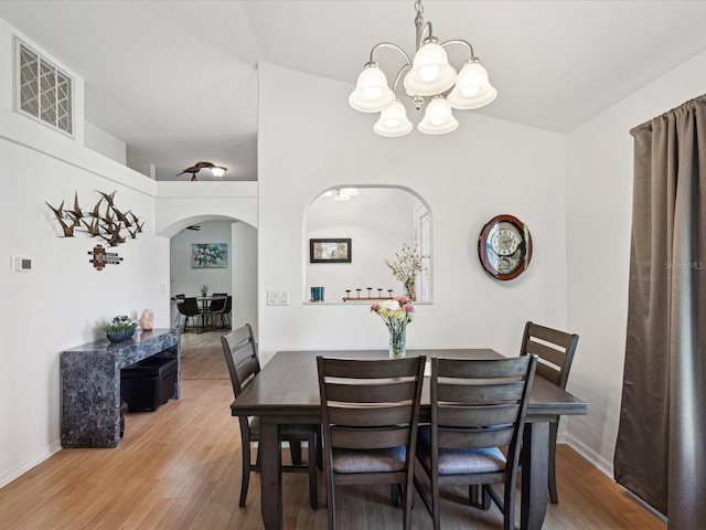 dining room featuring arched walkways, a notable chandelier, visible vents, wood finished floors, and baseboards