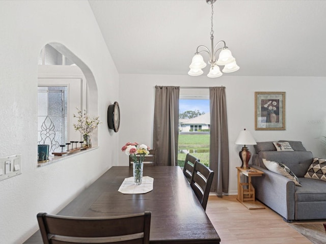 dining area with an inviting chandelier, light wood-style flooring, and vaulted ceiling