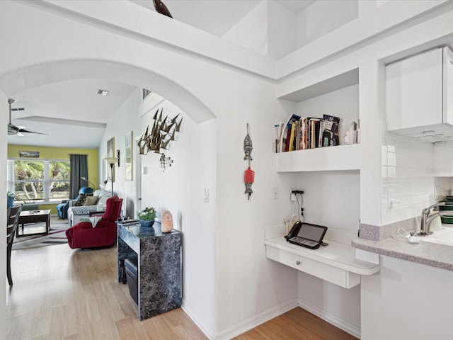 hallway featuring light wood-type flooring, arched walkways, and baseboards