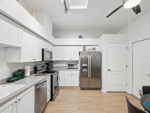 kitchen with light wood-style flooring, vaulted ceiling, stainless steel appliances, light countertops, and white cabinetry