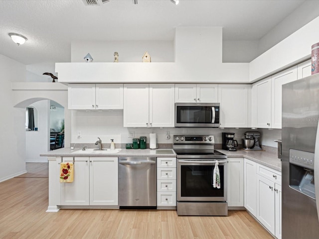 kitchen with stainless steel appliances, a sink, light wood-style flooring, and white cabinets