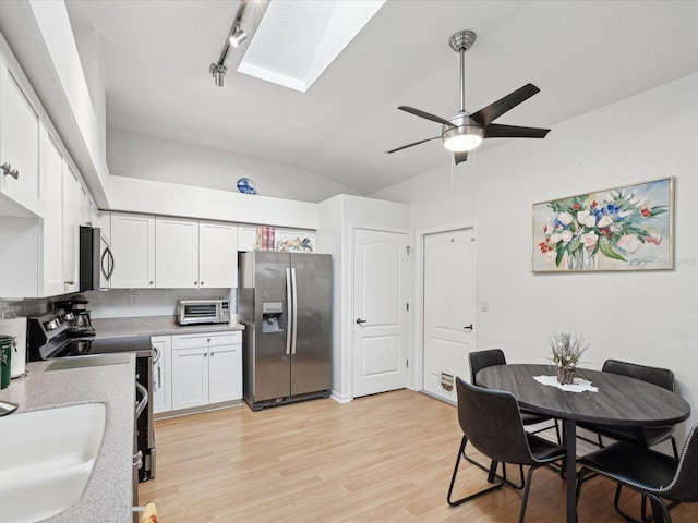 kitchen with stainless steel appliances, lofted ceiling with skylight, white cabinets, a sink, and light wood-type flooring