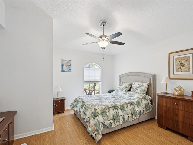 bedroom with a ceiling fan, light wood-style flooring, baseboards, and a textured ceiling