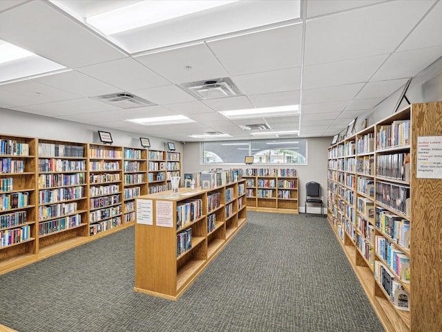 sitting room featuring carpet, visible vents, a paneled ceiling, and wall of books