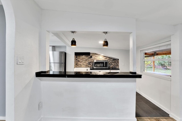 kitchen featuring backsplash, kitchen peninsula, hanging light fixtures, and appliances with stainless steel finishes