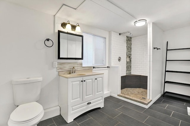 bathroom featuring toilet, a tile shower, and vanity