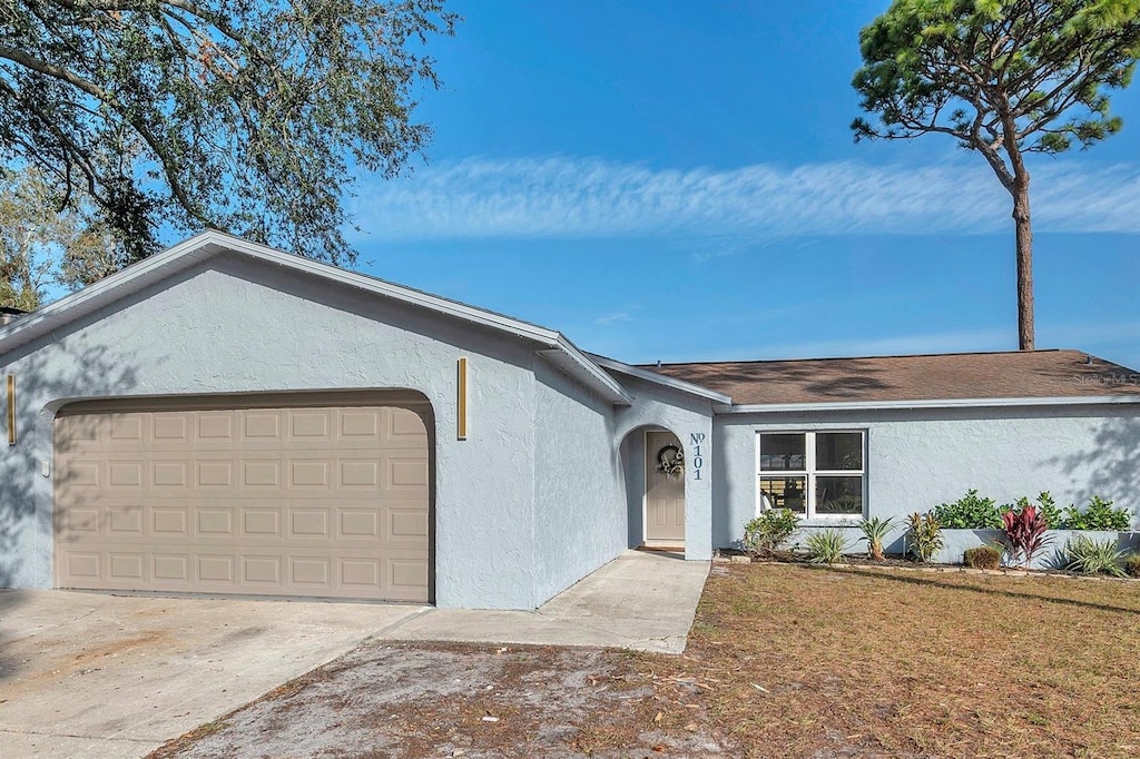 single story home with a front lawn, driveway, an attached garage, and stucco siding