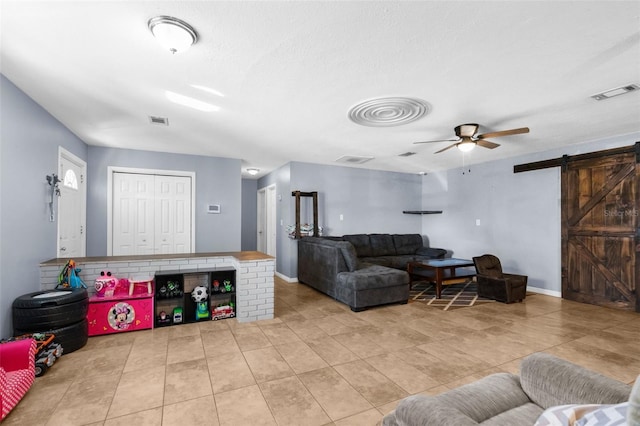 living room with ceiling fan, a barn door, and light tile patterned floors