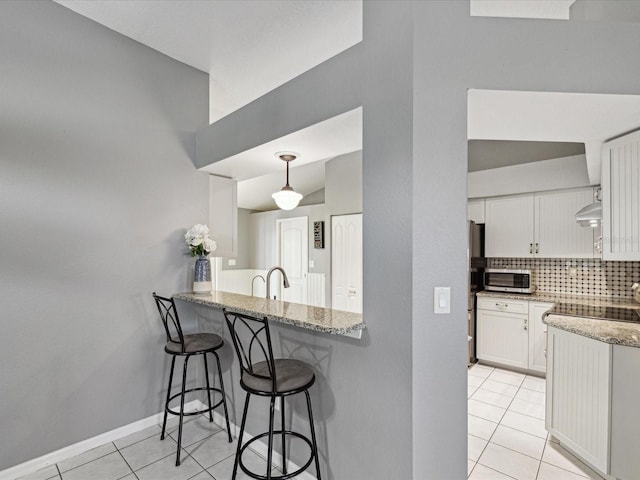 kitchen featuring backsplash, white cabinets, light stone countertops, a kitchen bar, and kitchen peninsula