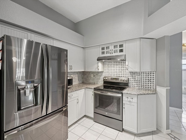 kitchen with light stone countertops, tasteful backsplash, light tile patterned flooring, white cabinets, and appliances with stainless steel finishes