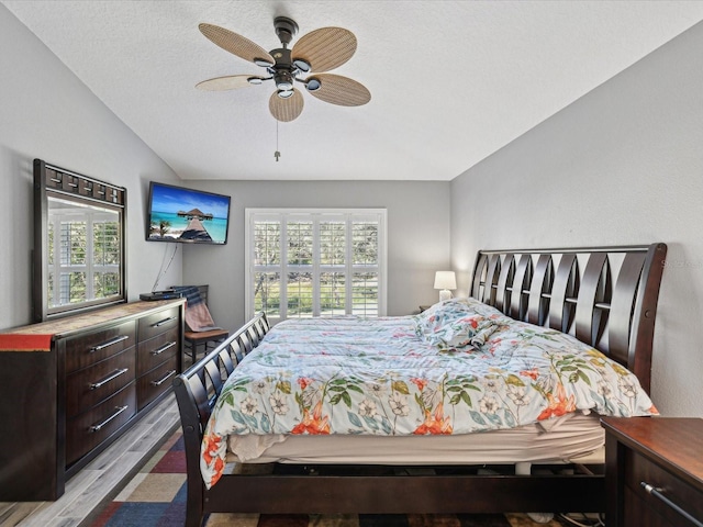 bedroom featuring a textured ceiling, ceiling fan, light hardwood / wood-style flooring, and vaulted ceiling